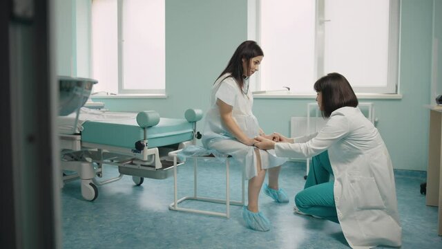 Close Up Of Pregnant Woman Suffering From Contractions While Medical Worker Holding Her Hands And Trying To Support. Professional Support For Future Mother At Modern Clinic.