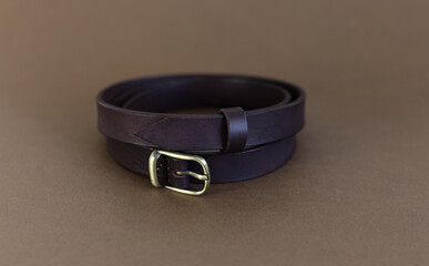 the eggplant-colored belt is handmade from genuine leather lying on a brown background