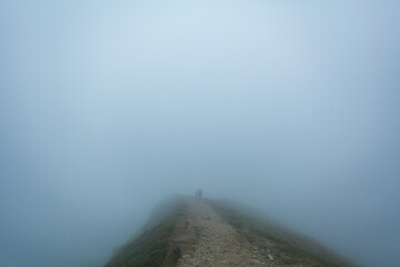 People walk in thick mist on a path on the hill, Ukrainian Carpathians
