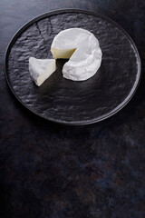 Camembert on a dark background. Soft cheese with white mold on a black plate. Minimalism. Copy space