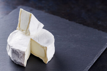 Camembert close-up on a dark background. Soft cheese with white mold on a slate board. Copy space