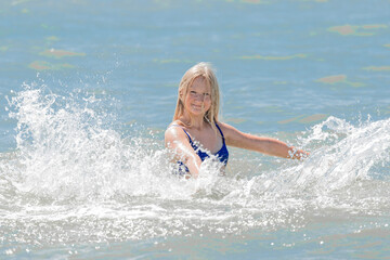 Young cheerful girl teenager blonde European appearance makes splashes of water with her hands in the sea