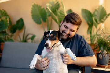 Young man holding his dog with a funny face and playing with him