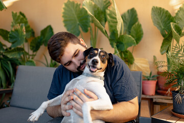 Young man holding his dog with a funny face and playing with him
