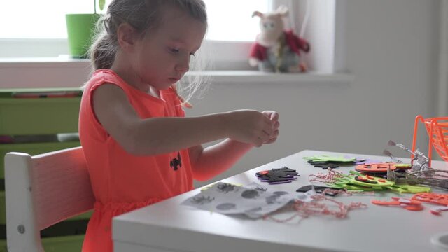 Cute little girl makes scenery for Halloween. A child makes pumpkins and spiders out of paper for Halloween.