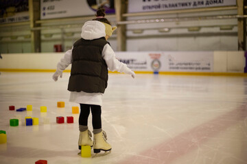 Little girl learns to skate. Children's skates. A child training on ice. The concept of children's...
