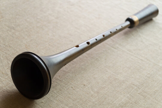 Shawm (schalmei, schalmeien) , a brown medieval wooden folk wind musical instrument with a metal decor, lies on a gray canvas