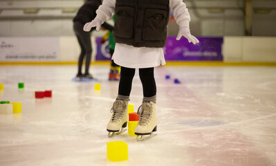 Little girl learns to skate. Children's skates. A child training on ice. The concept of children's...