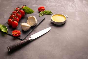 Cherry tomatoes mozarela and basil leaves on a chopping board with knife