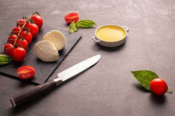 Obraz na płótnie Canvas Cherry tomatoes mozarela and basil leaves on a chopping board with knife