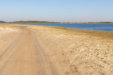 Dirty road with lake, sand and vegetation