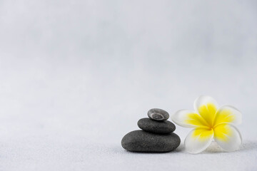 Fototapeta na wymiar Pyramids of gray and white zen pebble meditation stones on white background with plumeria tropical flower. Concept of harmony, balance and meditation, spa, massage, relax