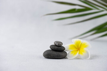 Fototapeta na wymiar Pyramids of gray and white zen pebble meditation stones on white background with plumeria tropical flower. Concept of harmony, balance and meditation, spa, massage, relax