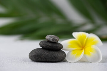 Obraz na płótnie Canvas Pyramids of gray and white zen pebble meditation stones on white background with plumeria tropical flower. Concept of harmony, balance and meditation, spa, massage, relax