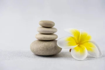 Foto op Canvas Pyramids of gray and white zen pebble meditation stones on white background with plumeria tropical flower. Concept of harmony, balance and meditation, spa, massage, relax © strigana