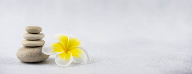 Fototapeta na wymiar Pyramids of gray and white zen pebble meditation stones on white background with plumeria tropical flower. Concept of harmony, balance and meditation, spa, massage, relax. Banner format