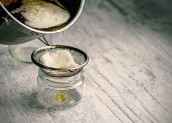The oil is filtered into a glass jar through a metal sieve and cheesecloth.