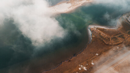 Aerial drone view from above of a dune beach shore line with morning sunlight and foggy clouds over...