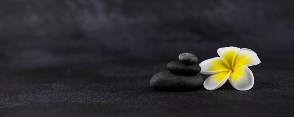 Fototapeta na wymiar Pyramids of gray and white zen pebble meditation stones on black background with plumeria tropical flower. Concept of harmony, balance and meditation, spa, massage, relax