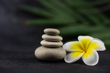 Foto op Canvas Pyramids of gray and white zen pebble meditation stones on black background with plumeria tropical flower. Concept of harmony, balance and meditation, spa, massage, relax © strigana