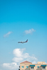front view, very far distance of a commercial passenger jet, landing on a tropical island, with condominiums lining the runway