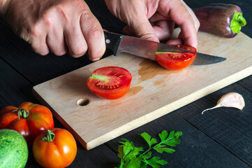 Chef is cutting a red tomato in a restaurant kitchen, a for a salad. Close-up of the hands of the cook during work on table.