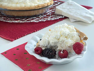 Coconut cream pie slice with berries in front of whole pie