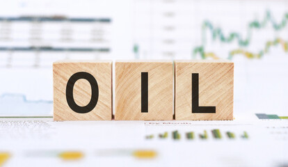 Word OIL made with wood building blocks on background from financial graphs and charts.