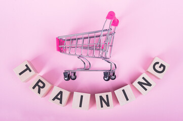 TRAINING - word on wooden cubes, on a pink background with a shopping trolley.