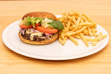 Beef burger with lettuce sprouts, melted cheese, red onion and tomato slices garnished with French fries