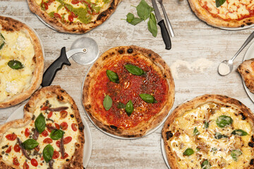 Top view image of assorted Italian pizzas with lots of basil, tomato, Parmesan cheese, wheat flour, pizza cutters and anchovies