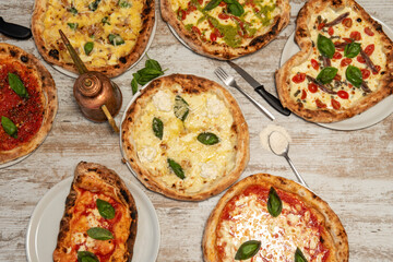 Top view image of assorted Italian pizzas with lots of basil, tomato, Parmesan cheese, wheat flour, pizza cutters and anchovies