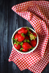 Photo of strawberries in a bowl on a black table with a checkered napkin