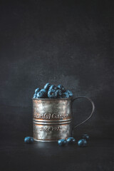 Photo of blueberries in a tin mug  on a table  a dark background