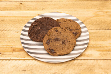 Gray and white striped plate with various flavored chocolate chip cookies on raw wooden table