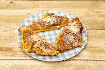 Delicious butter croissants with slices of almonds, syrup and icing sugar on raw wooden table