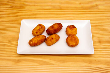 Serrano ham croquettes portion fried in olive oil on a white porcelain tray served in a Spanish tapas restaurant