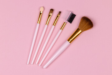 set of different makeup brushes close-up against a pink pastel background, top view