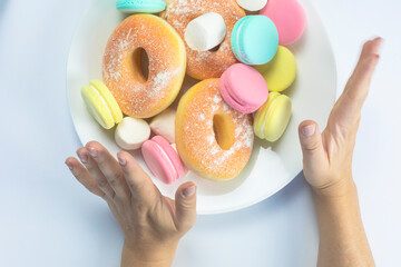Obraz na płótnie Canvas Woman hands making a hand sign of no and refuse for a white plate with fastfood and sugar, top view, healtcare and weightloss concept. donuts, macarons diet