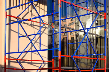 Prefabricated metal structure made of scaffolding, blue and red, against the background of the facade being repaired. Technologies and safety in construction. 