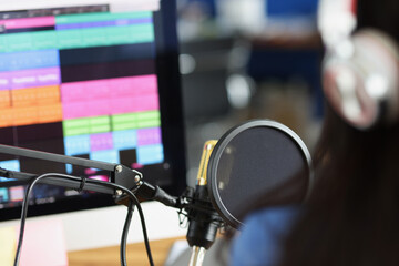 Woman in headphones in front of microphone looks at monitor with sound track