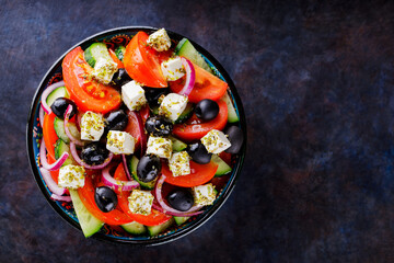 Greek salad in a bowl on a dark background. Healthy salad with feta cheese and olives. Fresh vegetable salad of Mediterranean cuisine. Copy space. Top view