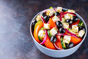 Classic Greek salad with feta and olives on a dark background. Diet and healthy mediterranean salad. Copy space. Top view