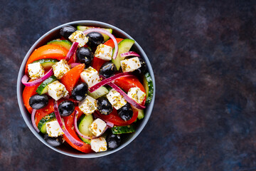 Classic Greek salad with feta and olives on a dark background. Diet and healthy mediterranean salad. Copy space. Top view