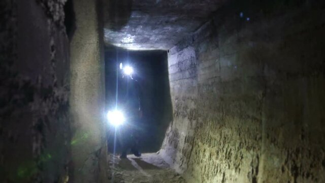 Underground tunnels. Exploration of grottos and caves. Walking on the ruins of concrete bunkers. Man with a flashlight passes through the old German military fortifications.