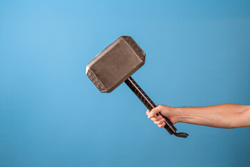 Be a hero, perform a feat. The Scandinavian hammer of Thor, Mjolnir in a man's hand. Photo on a blue background - obrazy, fototapety, plakaty
