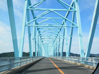青空のような真っ青に塗装されたトラス橋を通る風景