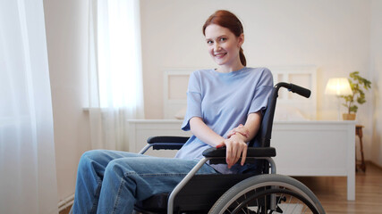 A young woman is sitting in a wheelchair and looking to the camera 