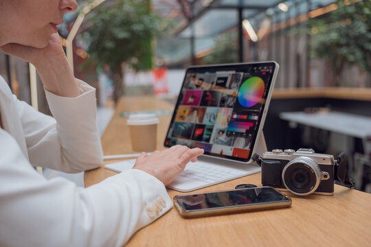 A photographer or retoucher works remotely with a laptop in a public space or coworking. A young woman in a white jacket works with images, a designer or a social media manager