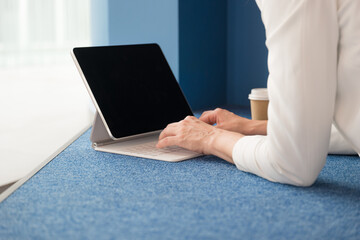 young freelance woman is sitting with a laptop in a public space and working on the Internet. Hands typing on the keyboard of a white thin laptop, close-up